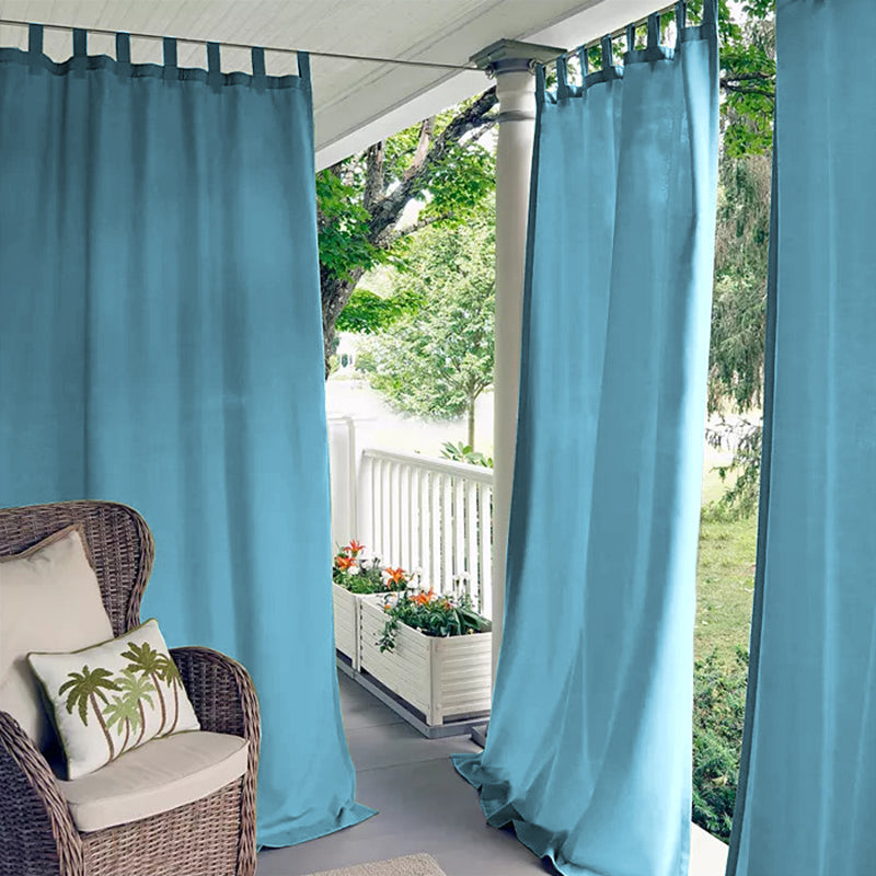 Porch deck with blue waterproof tab top outdoor curtains offering privacy & sun protection, beside a wicker chair.