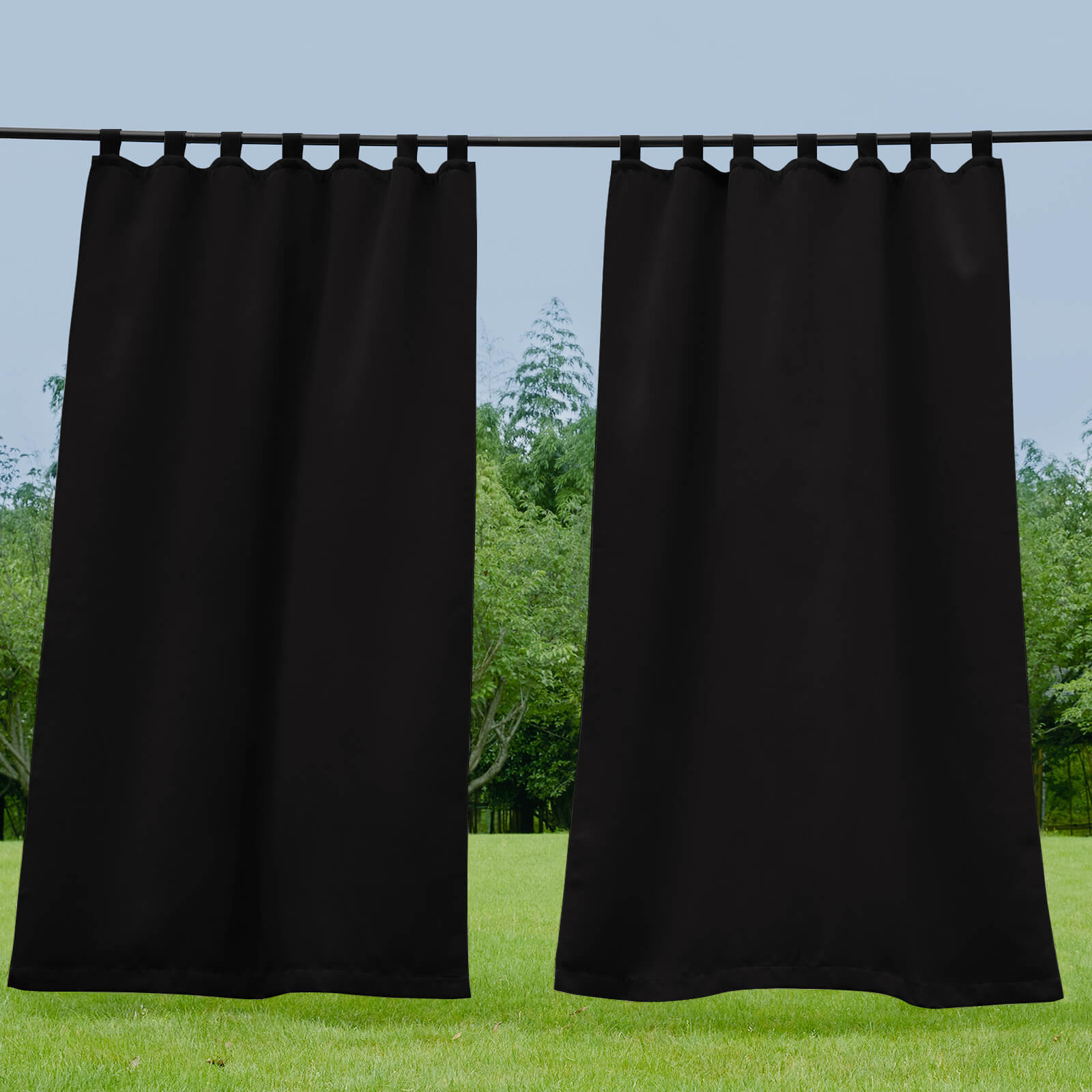 Black waterproof tab top outdoor curtains hanging on a rod over a green lawn and trees, ideal for porch or deck privacy.