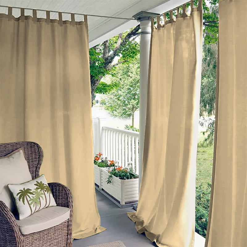 Beige tab top waterproof outdoor curtains providing privacy on a covered porch, next to a wicker chair.
