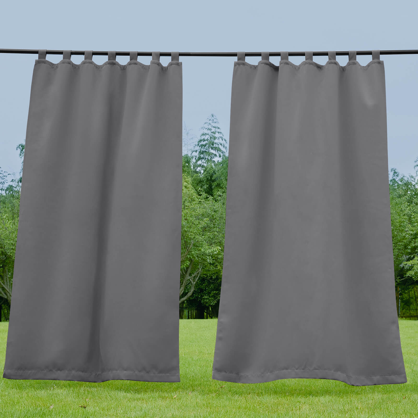 Pair of dark grey waterproof tab top outdoor curtains for porch or deck, showcasing weatherproof fabric in a garden.