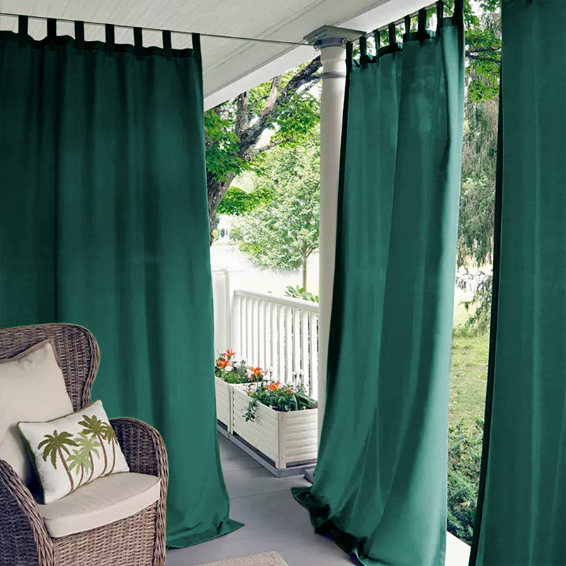 Emerald green tab top waterproof outdoor curtains on a porch deck, creating a private outdoor living space with a wicker chair.