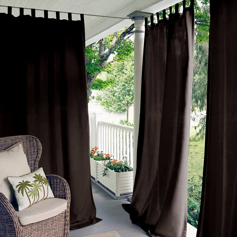Brown waterproof tab top outdoor curtains creating a private, shaded porch deck setting with a wicker chair.