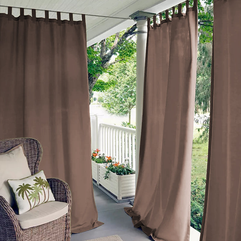 KGORGE brown tab top waterproof outdoor curtains on a porch deck, offering shade & privacy. Wicker chair, flowers, and trees.