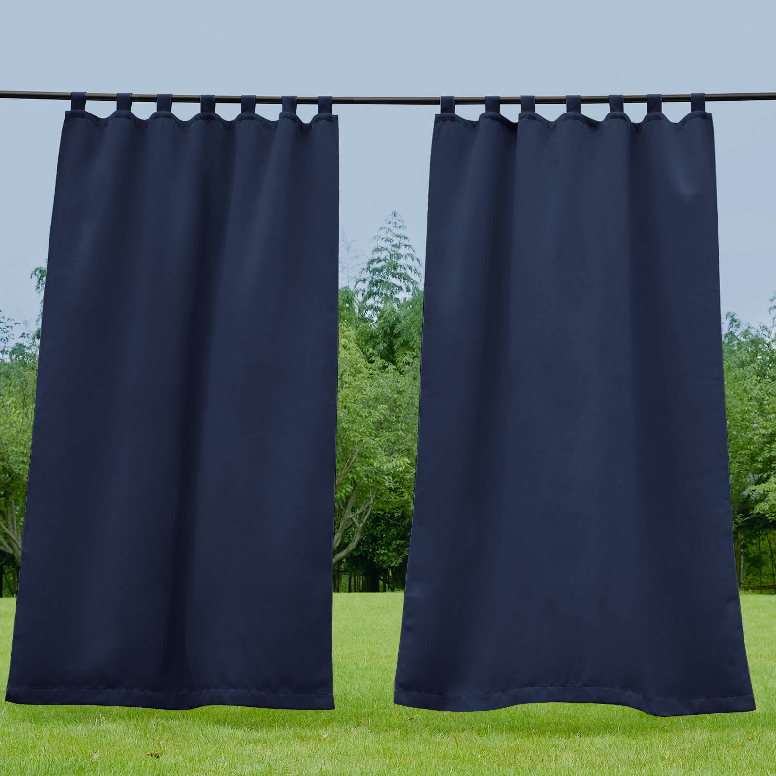 Two navy waterproof tab top outdoor curtains on a rod, offering patio privacy and shade against a sunny green landscape.