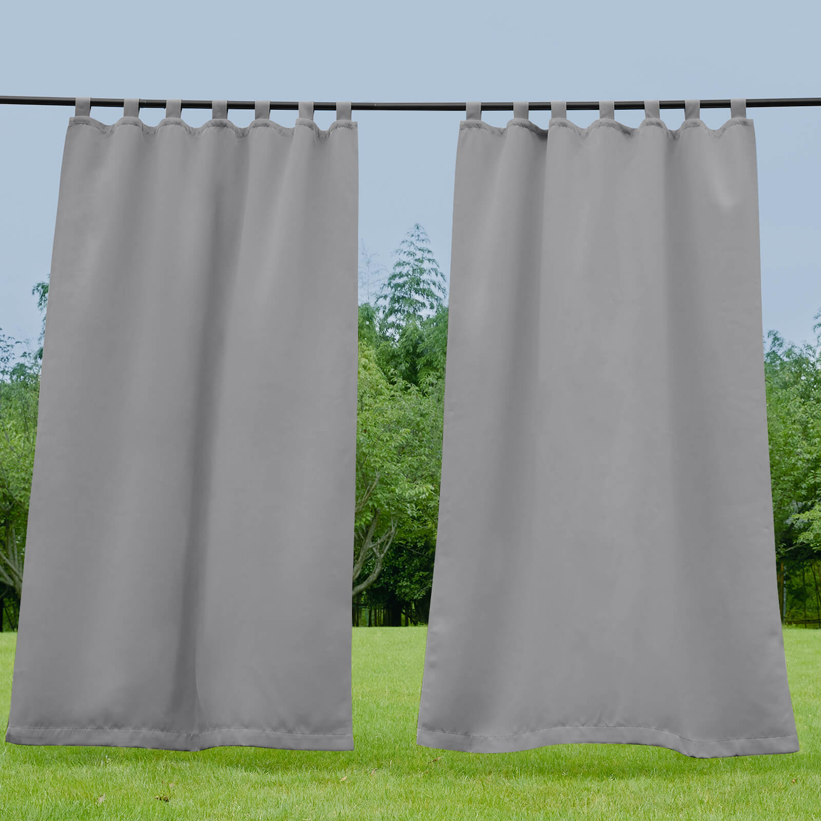 Two gray waterproof tab top outdoor curtains on a rod, slightly open with a green lawn and trees in the background.