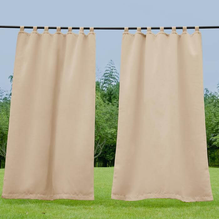 Beige waterproof tab top outdoor curtains panels hanging outdoors, offering shade and privacy for a porch or deck.