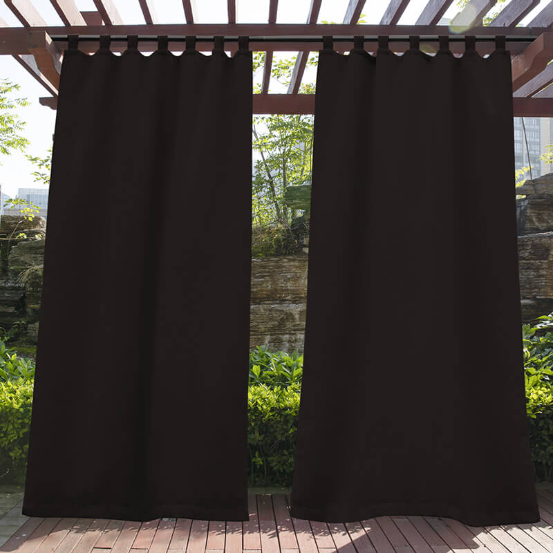 Two dark brown waterproof tab top outdoor curtains hanging from a wooden pergola, providing privacy for a porch deck.
