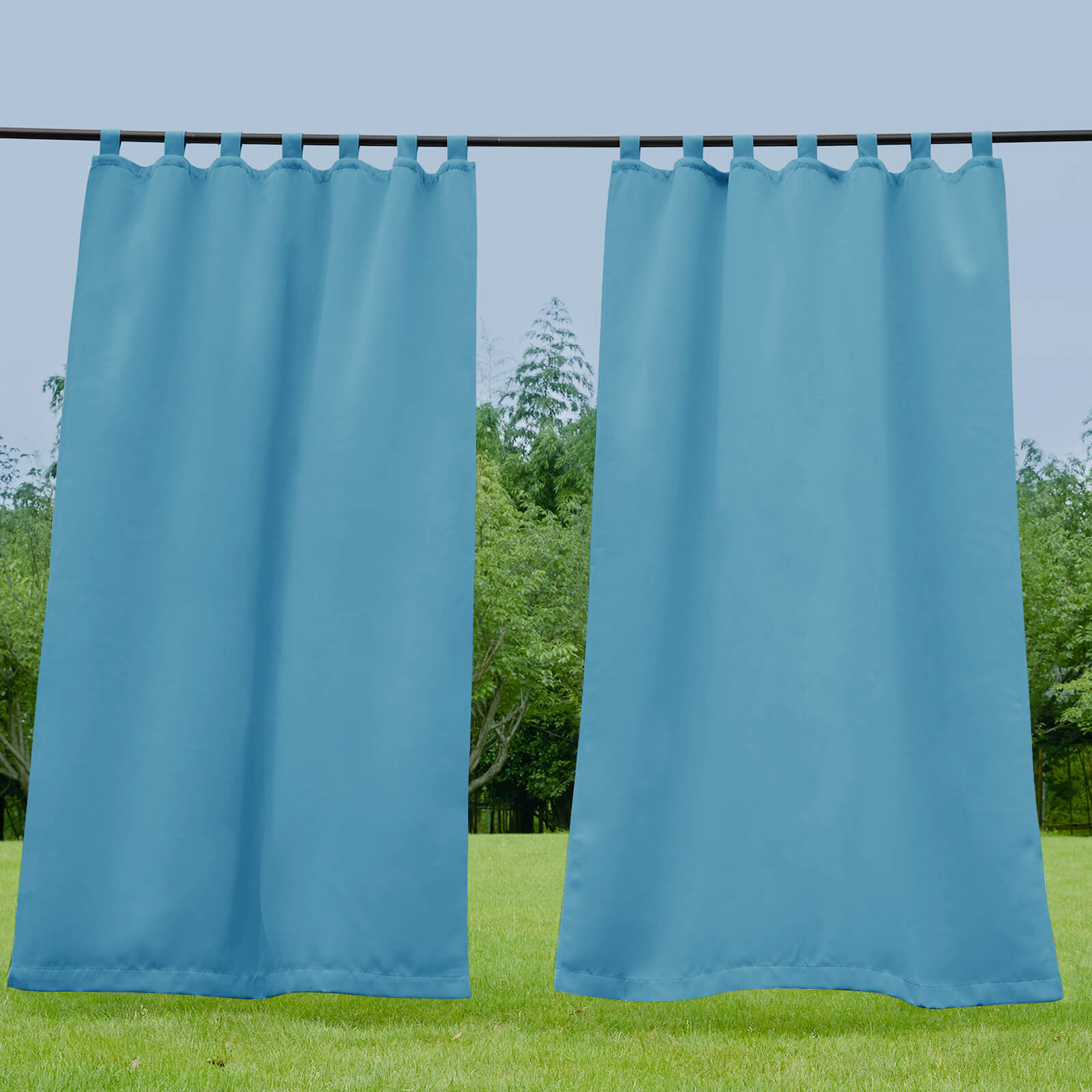 Teal blue waterproof tab top outdoor curtain panels for porch or deck, hung on a rod with lush green trees in background.