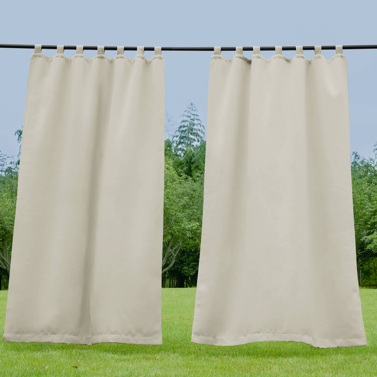 Light beige waterproof tab top outdoor curtains hanging on a rod against green trees & blue sky, ideal for porch or deck.