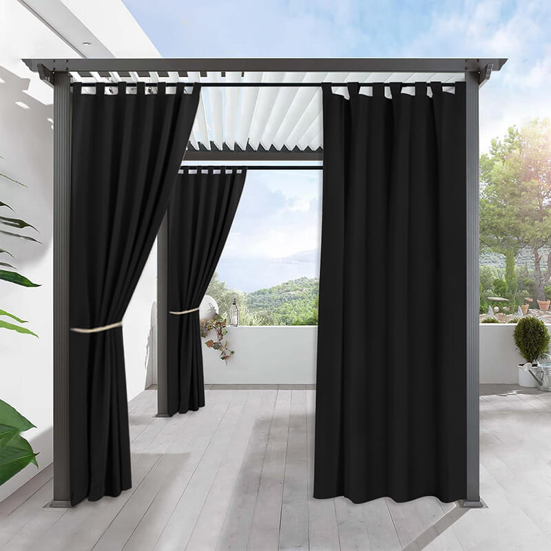 Black waterproof tab top outdoor curtains on a modern porch deck pergola. One panel closed, others tied back revealing a scenic view.