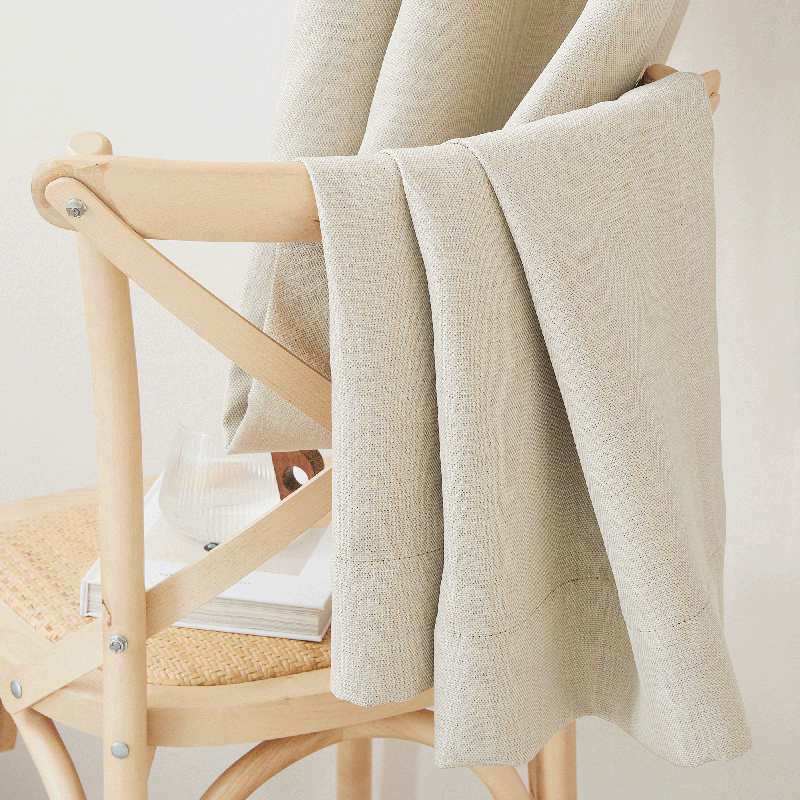 Close-up of textured, light beige blackout curtain fabric draped over a wooden chair, perfect for living room & bedroom.