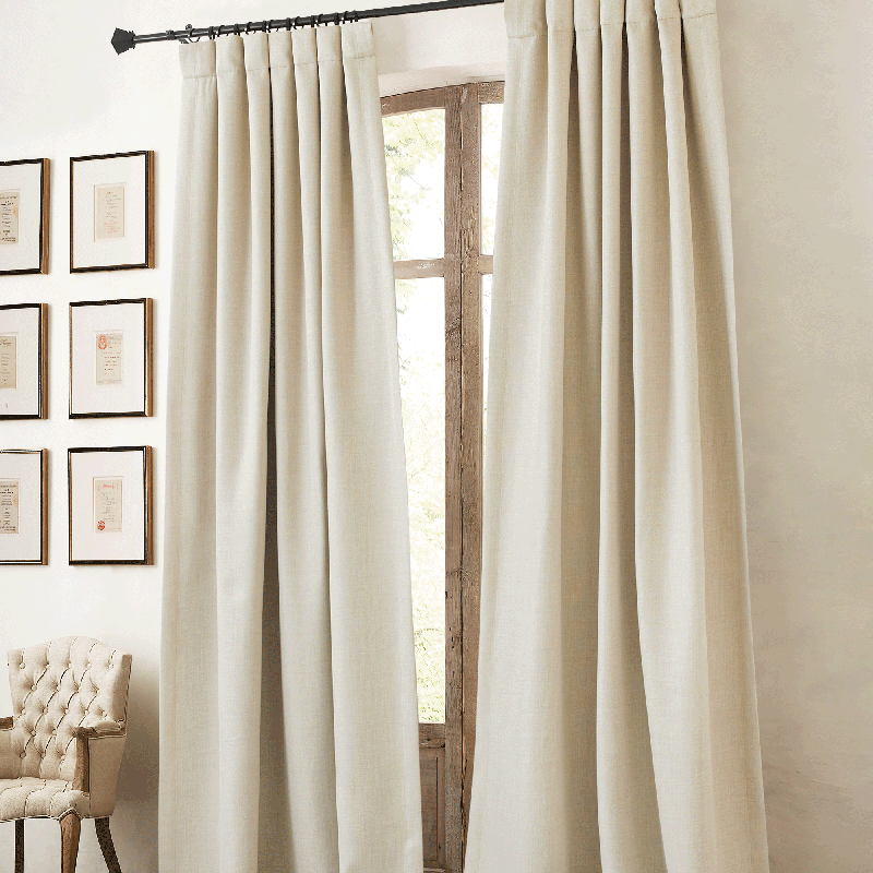 Two panels of plain beige blackout curtains with rod pocket and back tab, styled in a living room window.