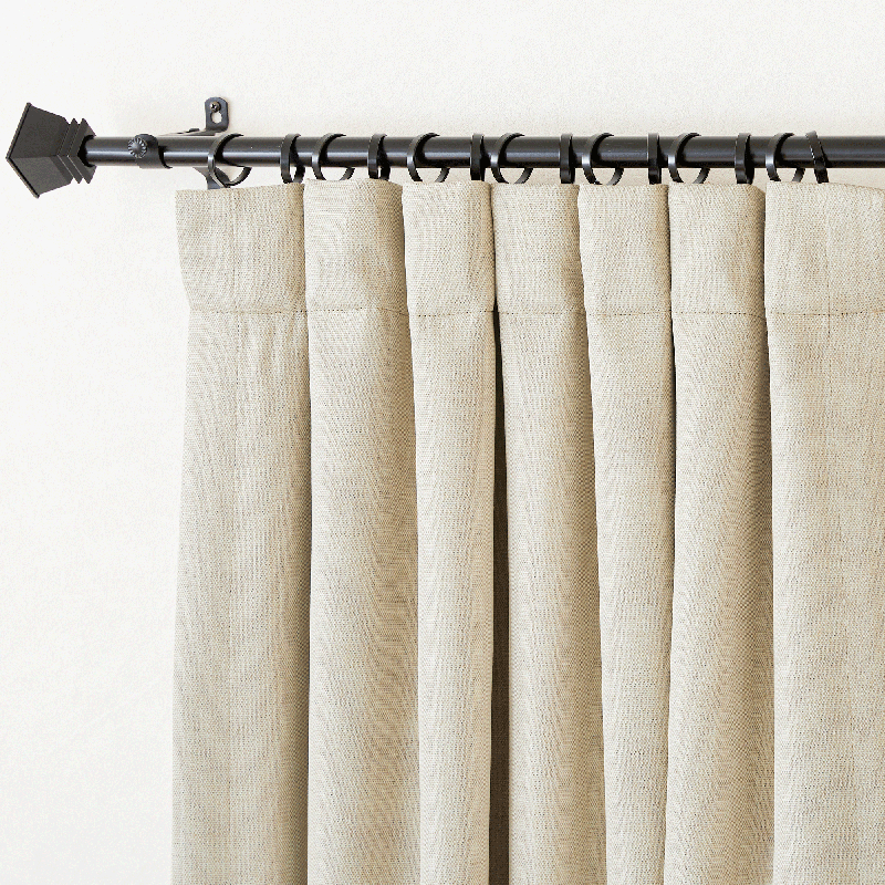Textured plain beige blackout curtain with back tab hanging, neatly pleated on a black rod, showing fabric detail.