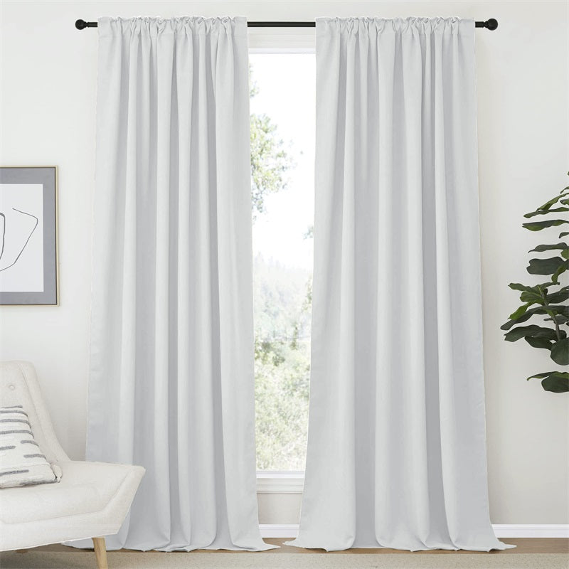 Two white rod pocket blackout curtain panels in a living room, blocking light from a window.