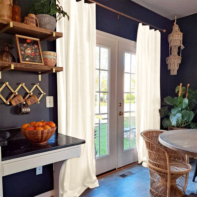 Pair of cream velvet Rod Pocket & Back Tab blackout curtains framing glass french doors in a cozy living room.