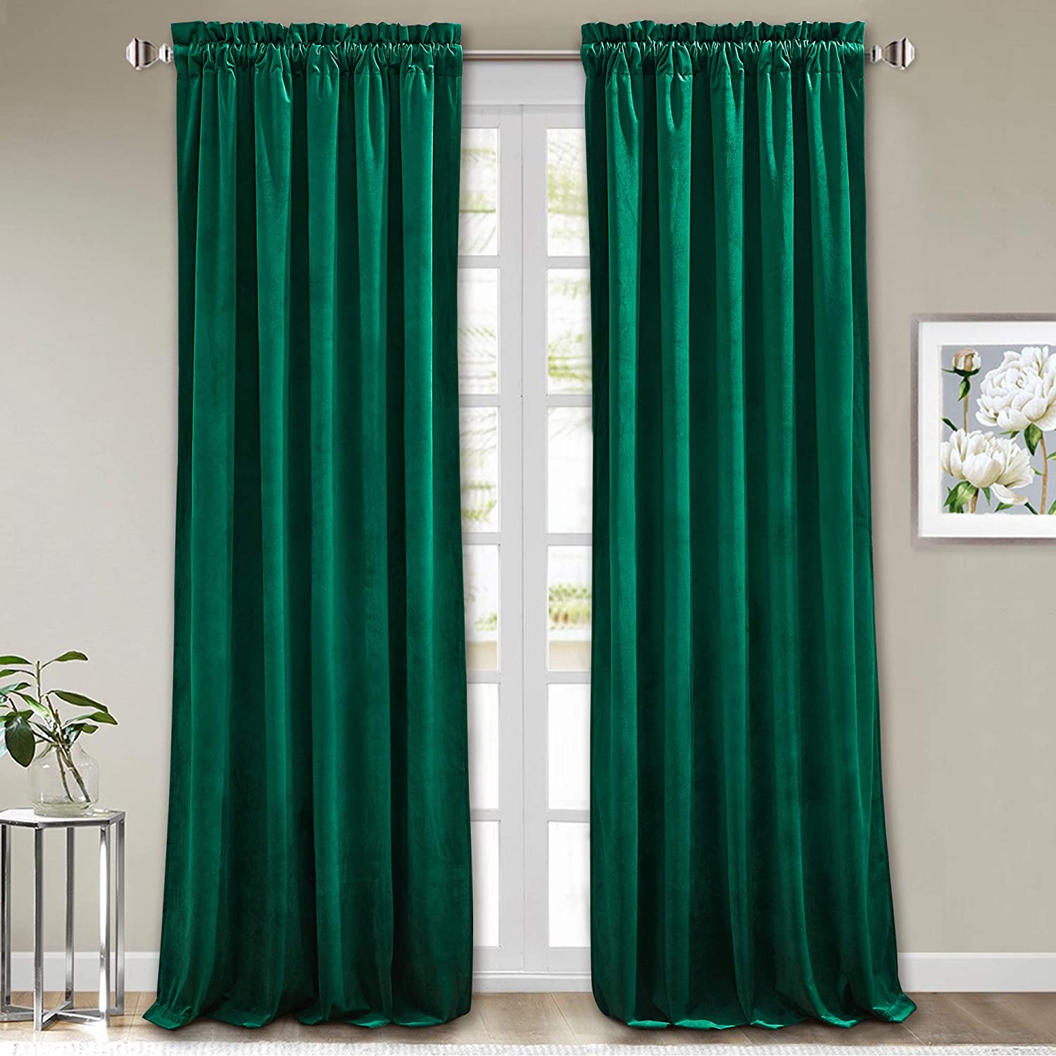 Two emerald green rod pocket velvet blackout curtains covering a living room window. Noise reducing panels with luxurious texture.