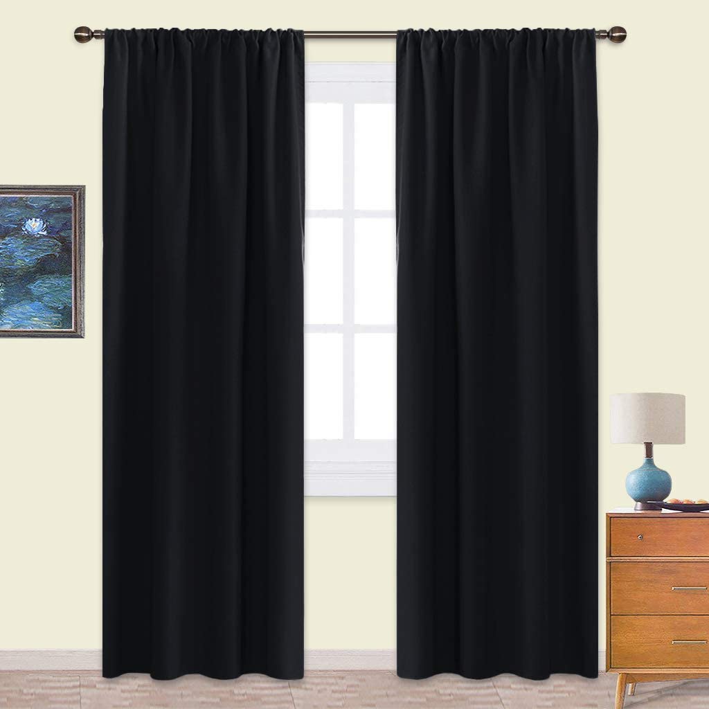 Two black rod pocket triple weave blackout curtains hanging on a window in a living room or bedroom setting