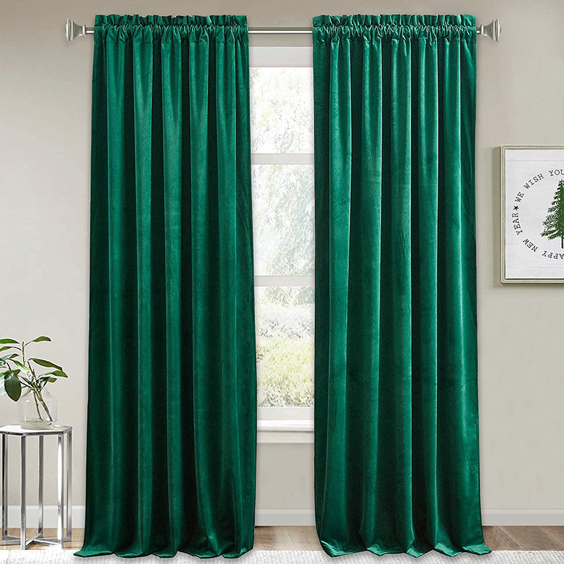 Two rich green velvet rod pocket blackout curtains hanging in a window, ideal for luxury living room or bedroom privacy.