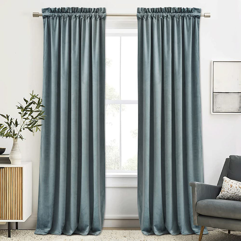 Pair of plush blue velvet rod pocket curtains on a metal rod, ideal for luxury noise reducing blackout in living rooms or bedrooms.