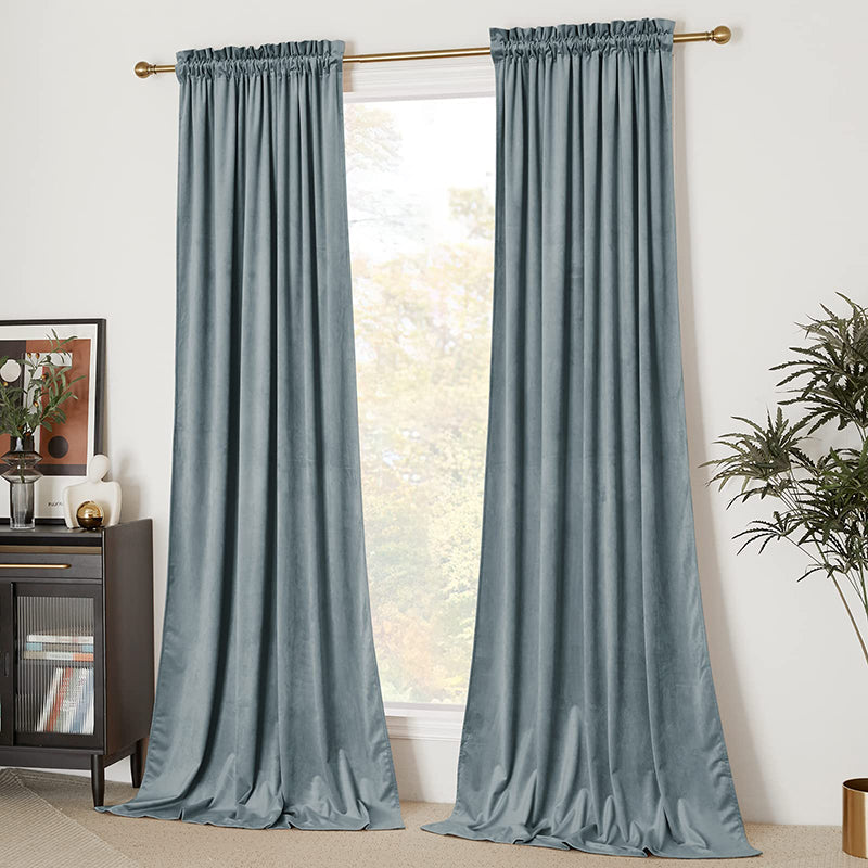 Two dusty blue velvet rod pocket blackout curtain panels hanging in a living room window, offering privacy and light blocking.