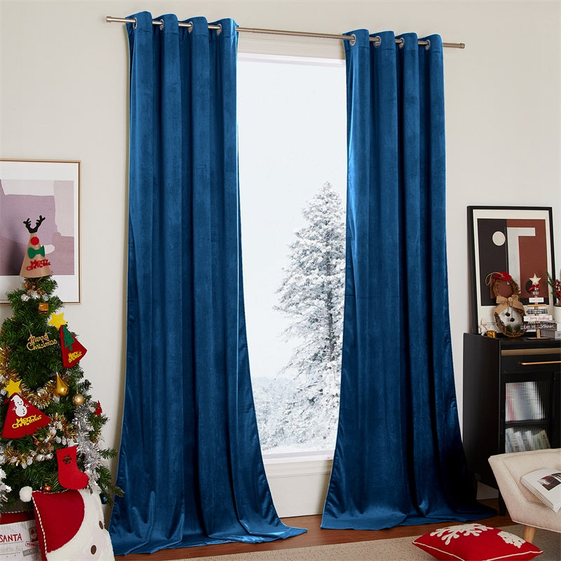 Plush deep blue velvet blackout curtains with silver grommets covering a living room window, with a snowy tree and Christmas decor.