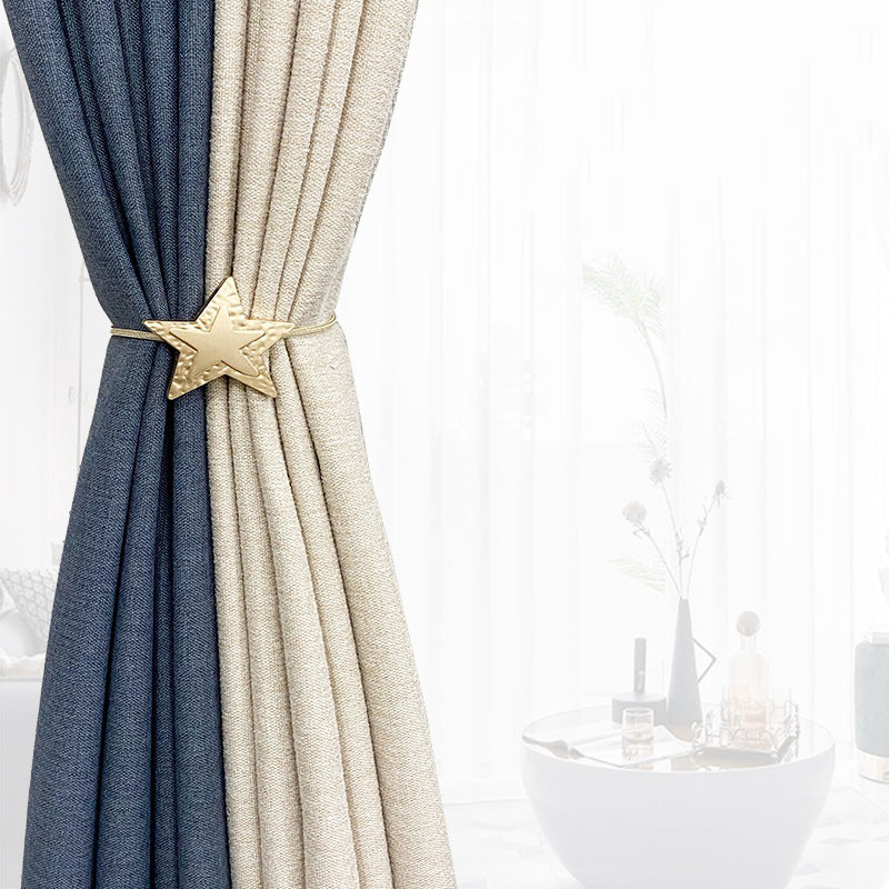 Close-up of a two-tone navy and beige outdoor curtain held by a decorative gold metal star magnetic tieback.