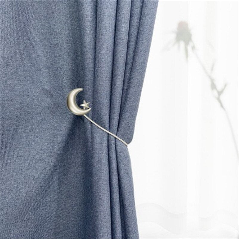 Silver metal moon and star magnetic curtain tieback strap holding a pleated blue curtain panel elegantly.