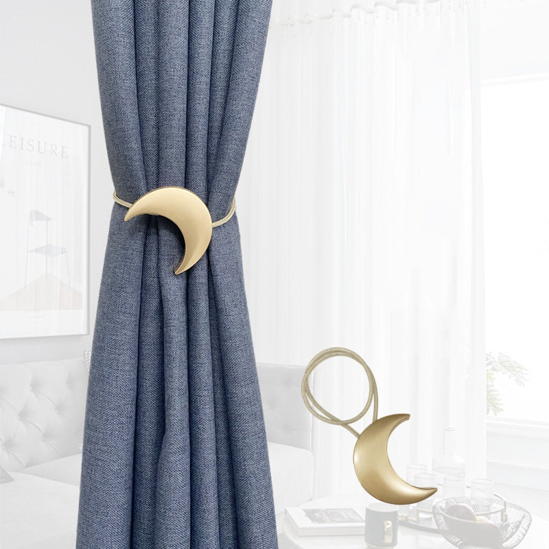 Golden crescent moon metal magnetic curtain tieback holding back a blue outdoor curtain. Another celestial moon tieback is displayed untied.