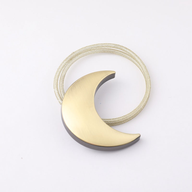 Brushed gold crescent moon metal magnetic curtain tieback with a light woven cord strap for securing drapes or outdoor curtains.