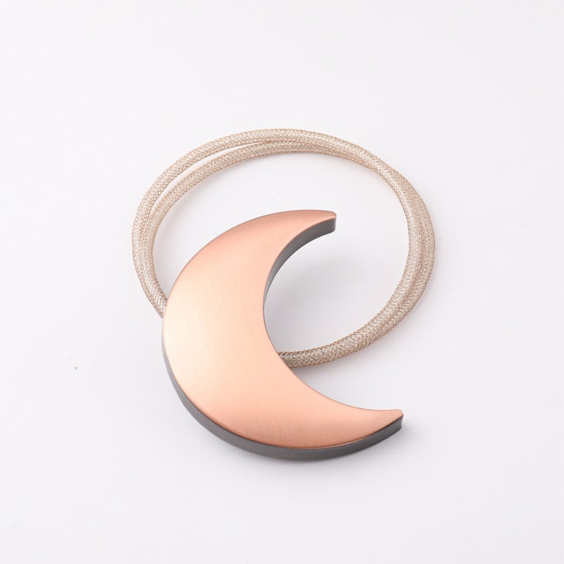 Decorative metal moon magnetic curtain tieback with a rose gold finish and light braided cord, perfect for outdoor patio curtains.