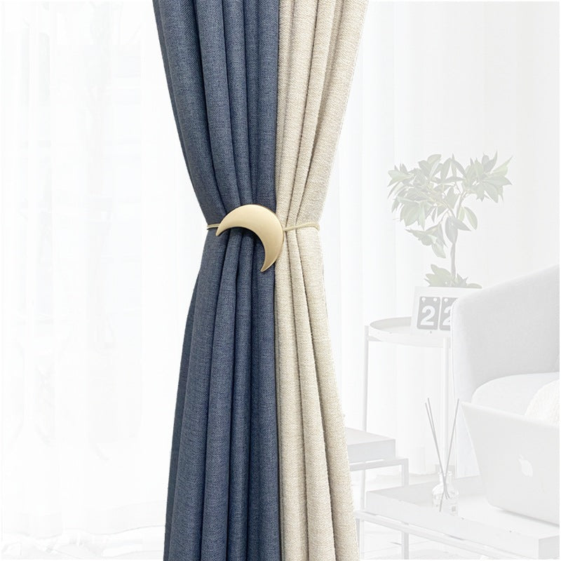 Gold crescent moon metal magnet curtain tieback securing blue and beige curtain panels.