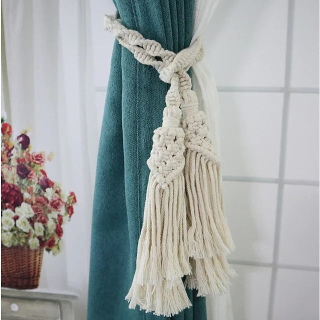 Hand woven cream macrame rope tieback with tassels holding a teal curtain, a stylish window treatment accessory.