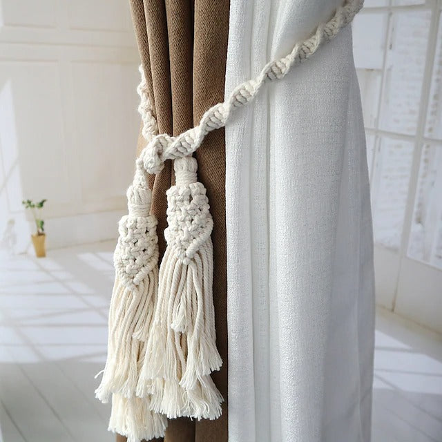 Hand woven cream macrame tassel tieback for curtains, securing brown and white drapes as a stylish window treatment.